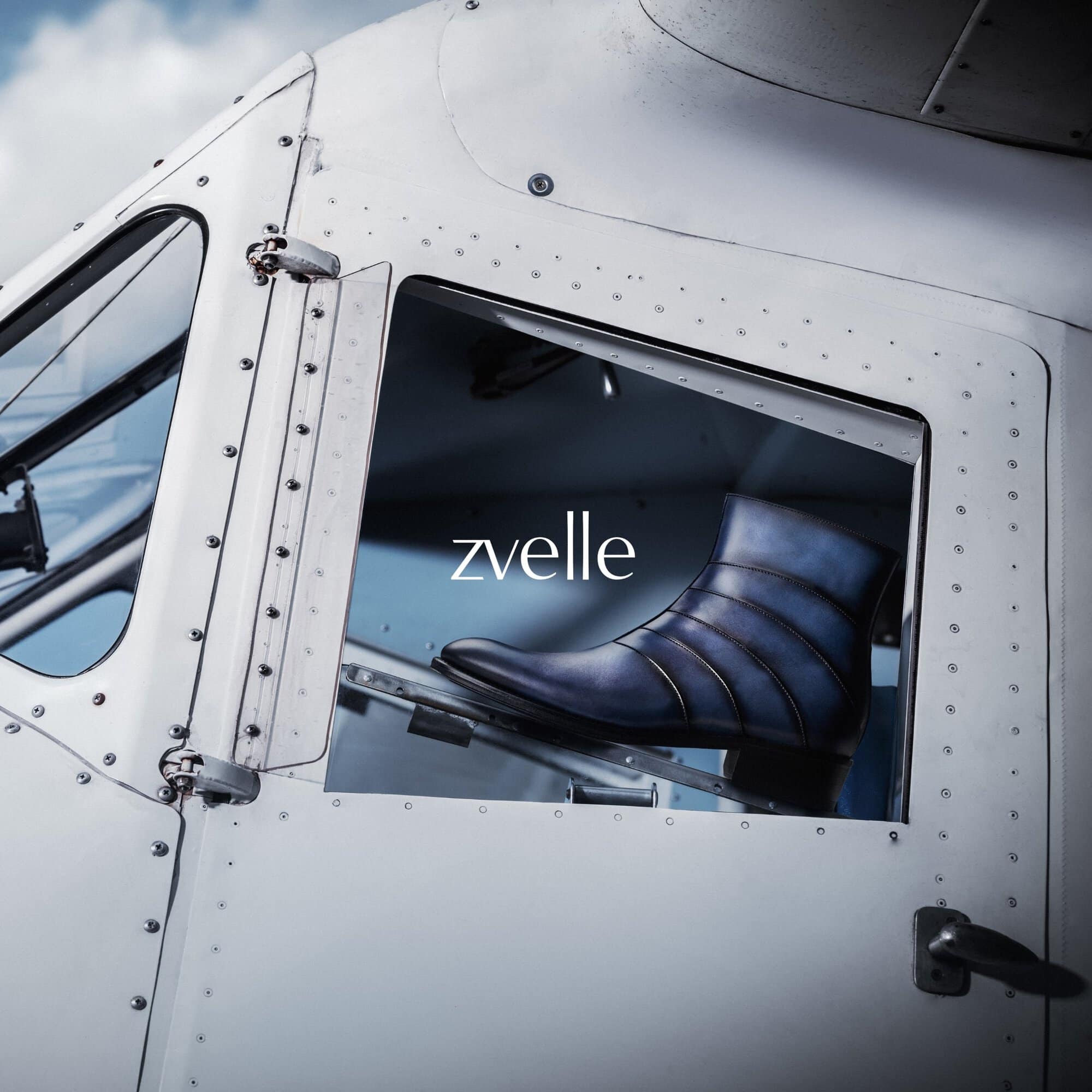 Blue leather ankle boot displayed inside the window of a white aircraft fuselage for the Zvelle Alatus campaign.