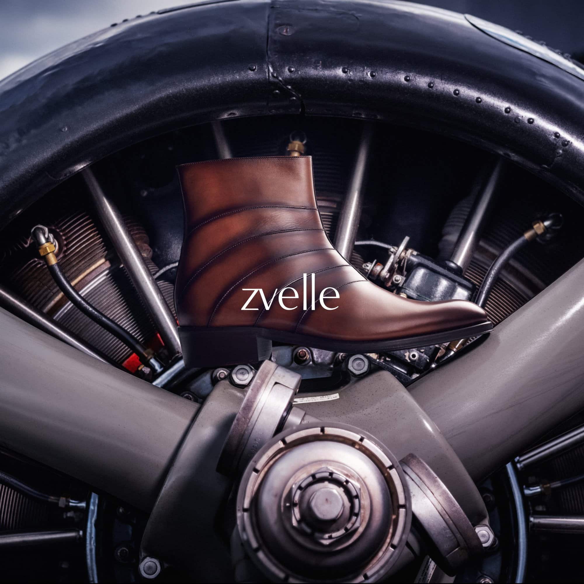 Brown leather ankle boot resting on an airplane engine with zvelle branding across the side