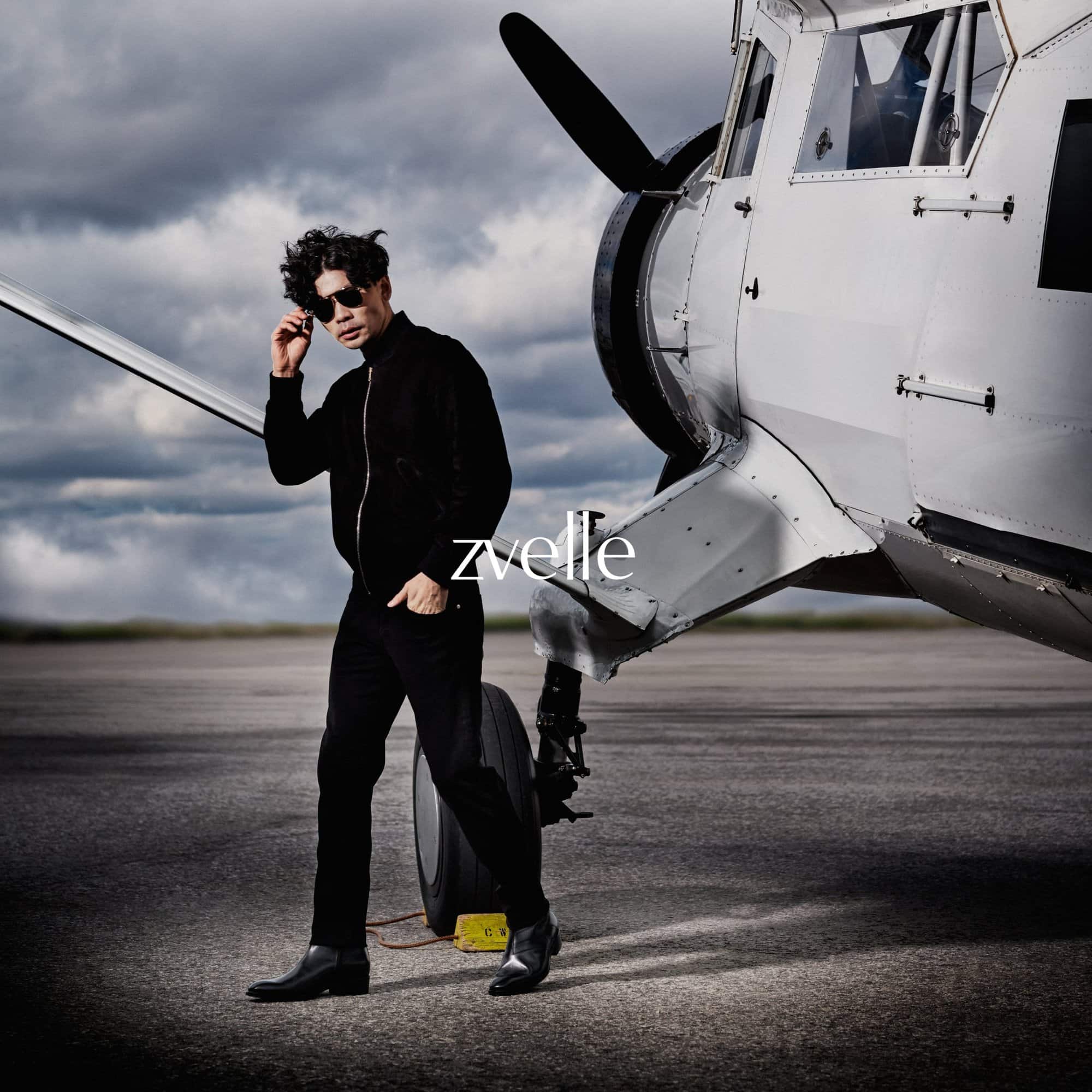 Man wearing sunglasses and black jacket standing in front of a white airplane on an airfield