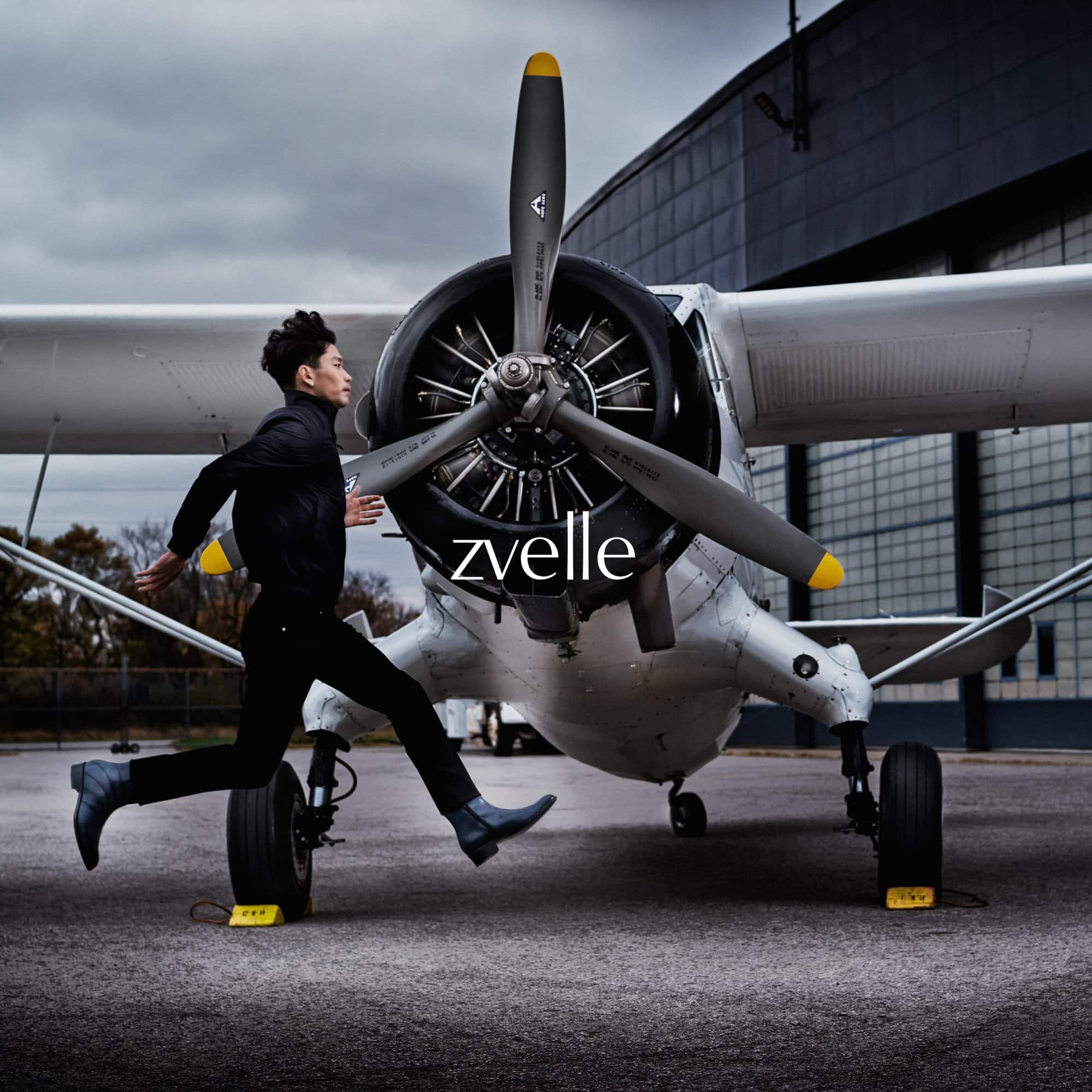 Man running past a parked vintage white airplane on an outdoor tarmac for the Zvelle Alatus campaign.