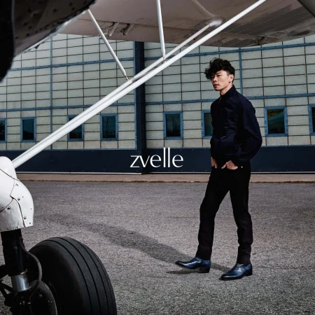 Man wearing dark jacket and trousers standing near an airplane wing and wheel on an airfield