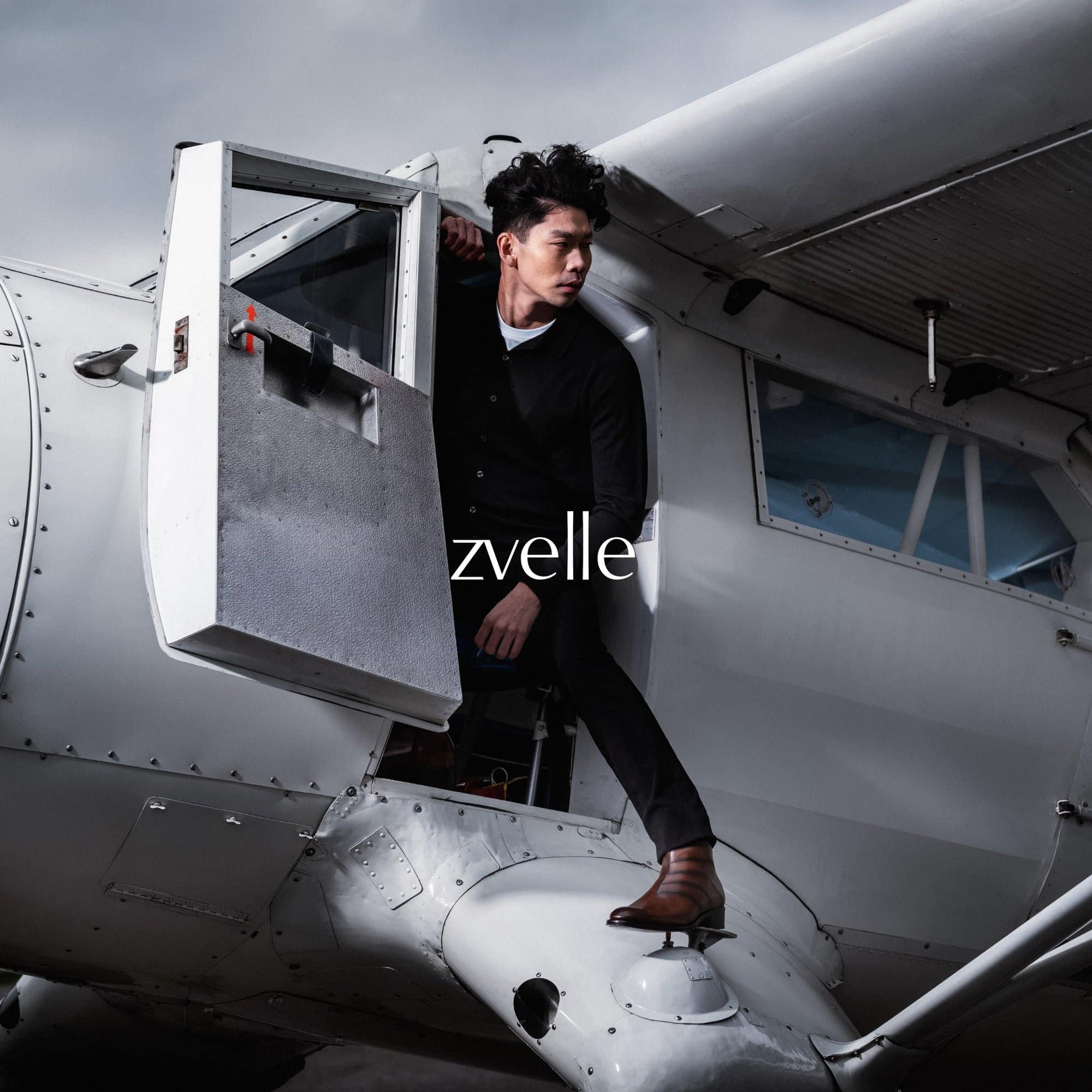 Man wearing black shirt and brown leather boots stepping out of a white aircraft door.
