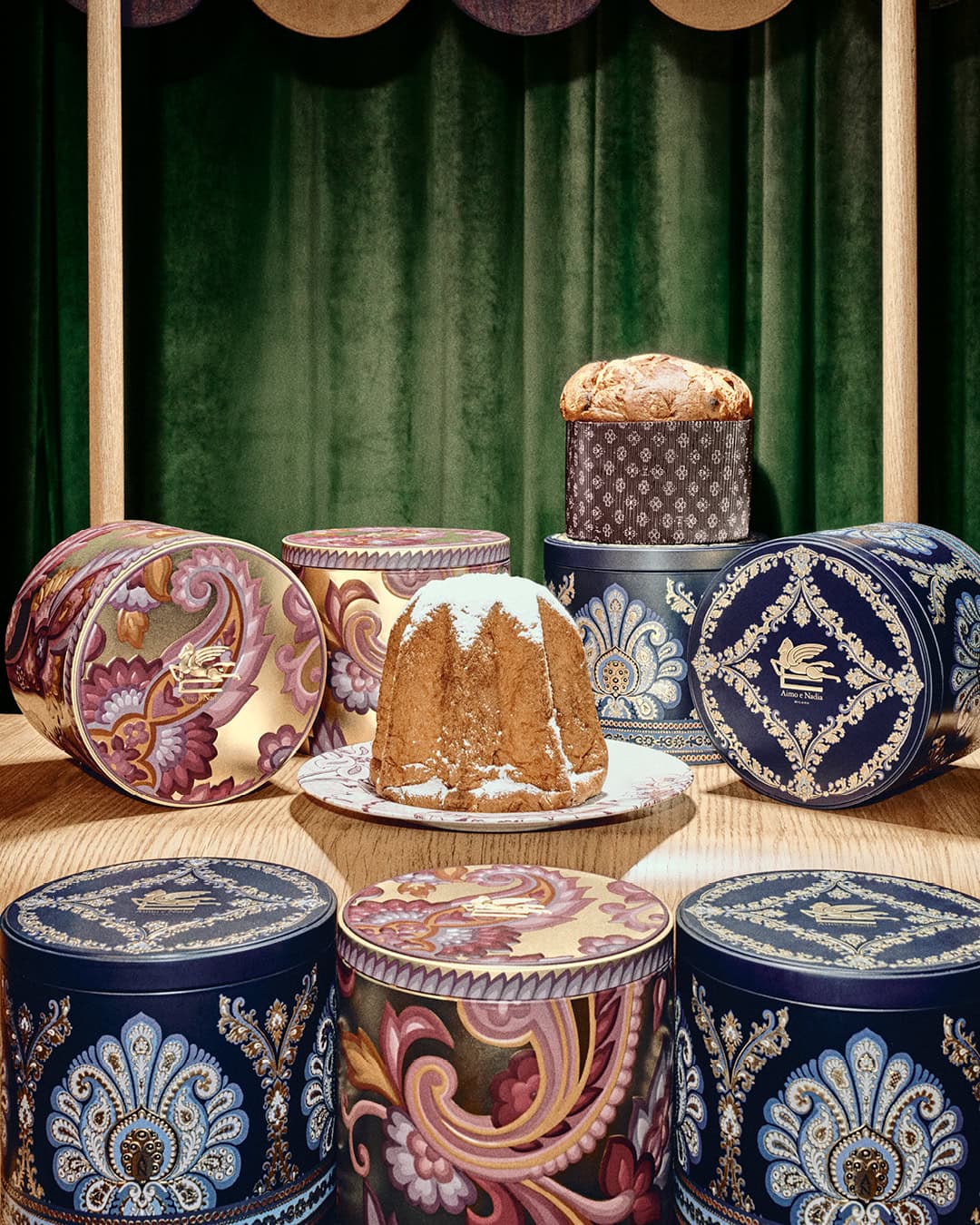 Panettone and pandoro cakes arranged with decorative patterned gift boxes against a green curtain background