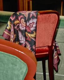 Close-up of patterned silk scarf draped over red velvet chair back in theater interior