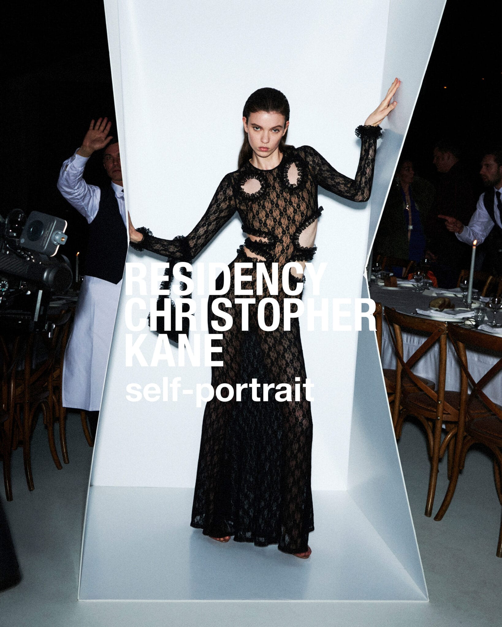 Model wearing a long black lace dress posing inside a white illuminated sculptural structure at a dinner event.