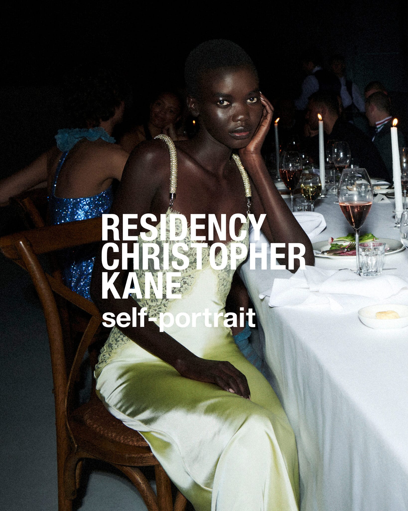 Black model wearing a pale green satin dress seated at a candlelit dinner table for Self-Portrait.
