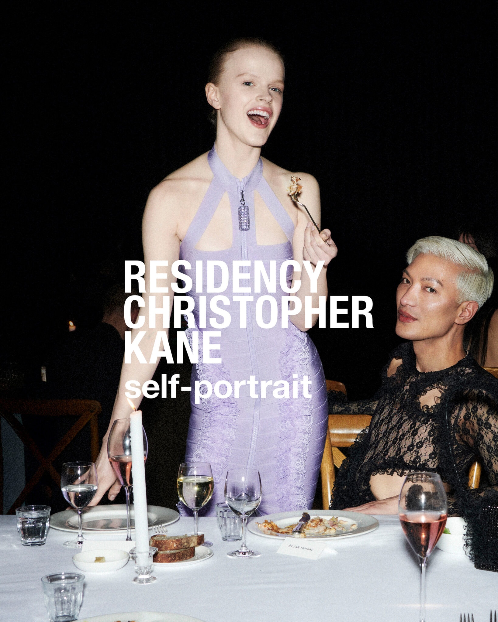 A woman in a fitted lavender halter dress holding a fork at a dinner table alongside another person wearing black lace.