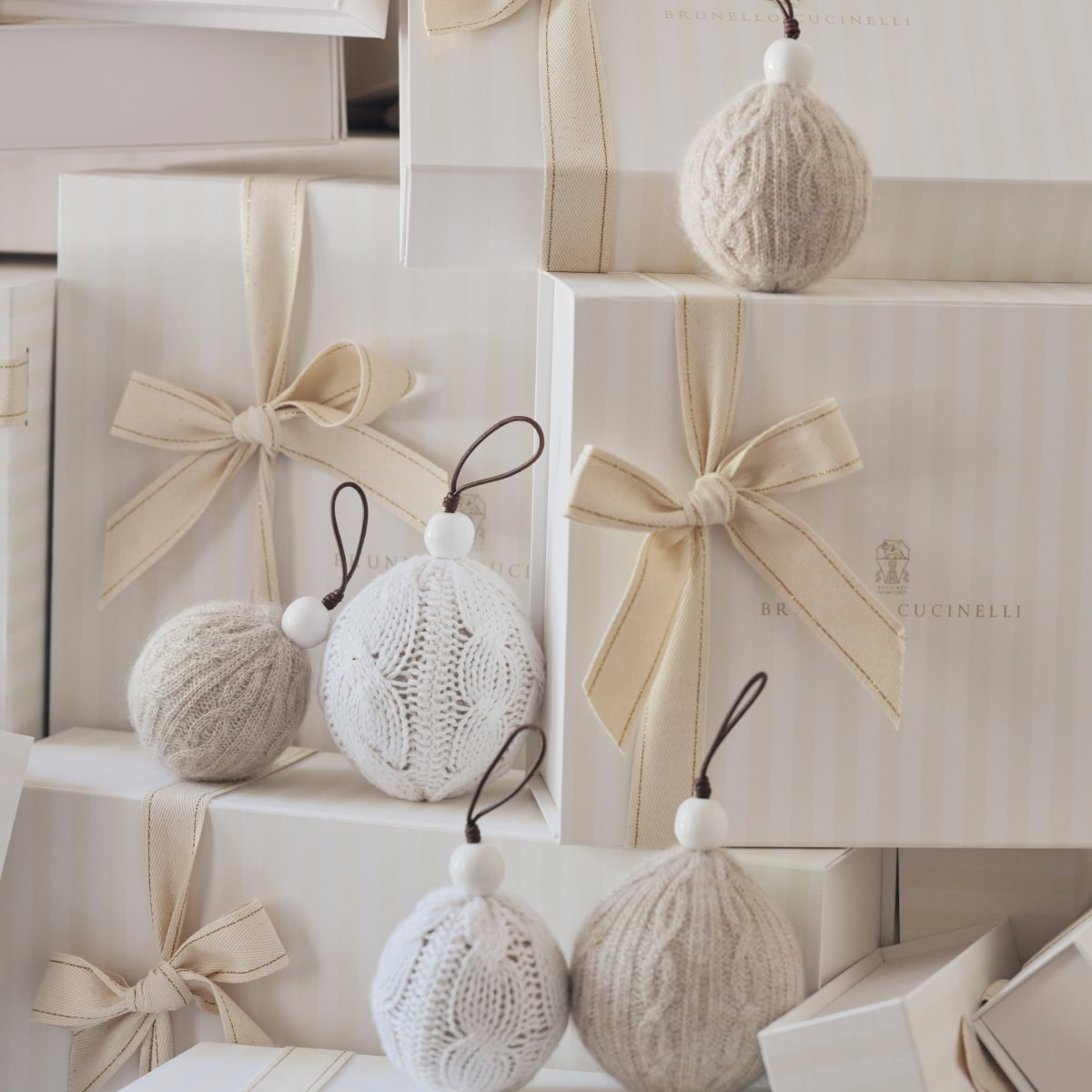 Stacked white gift boxes tied with cream ribbons alongside knitted ball ornaments for Brunello Cucinelli.