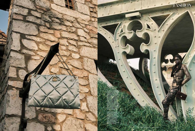 Fashion editorial shot with a black woman leaning against a bridge wearing stylish clothing, and a Chanel purse hanging on a stone wall.