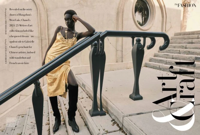 Fashion editorial shot of a Black model in a gold dress, leaning on a railing on stone steps with architectural details, bathed in soft light.
