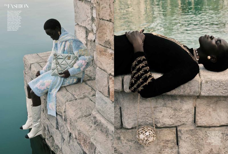 Fashion editorial showcasing two adult women wearing knit outfits, jewelry, and handbags near a stone wall by a waterfront.