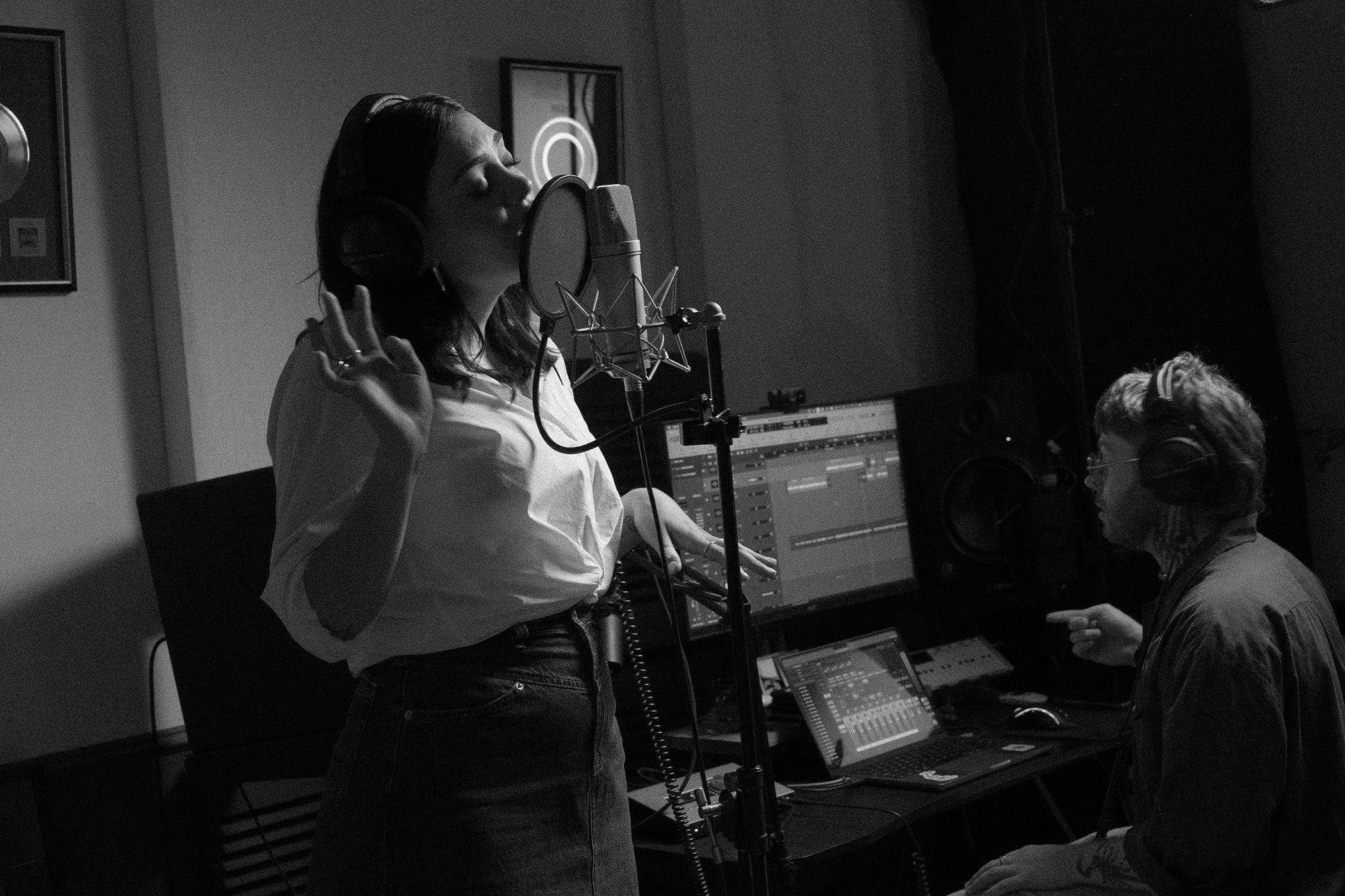 Thelma Plum wearing a white button-down shirt singing into a studio microphone in a recording studio for R.M. Williams