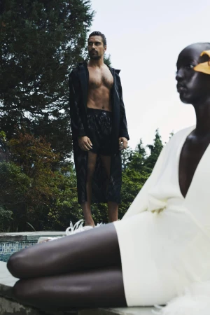 Models outdoors with Mark Vanderloo standing by trees and a seated figure in a white outfit by a pool for Taller Marmo.