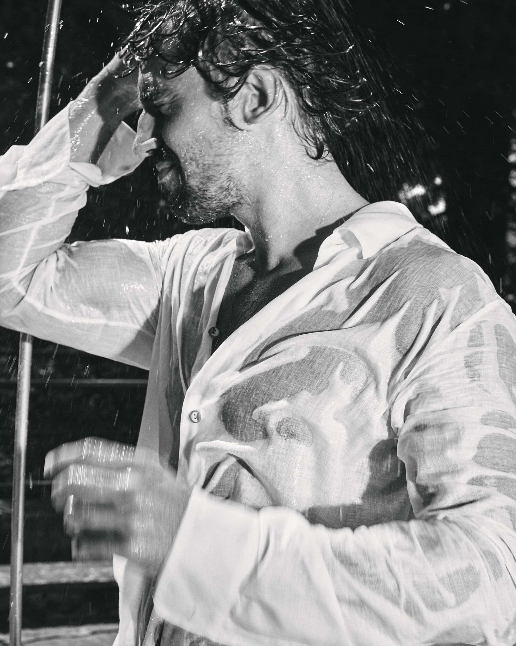 Man wearing a wet white shirt with water splashing around him in black and white