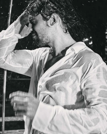 Man wearing a wet white shirt with water splashing around him in black and white