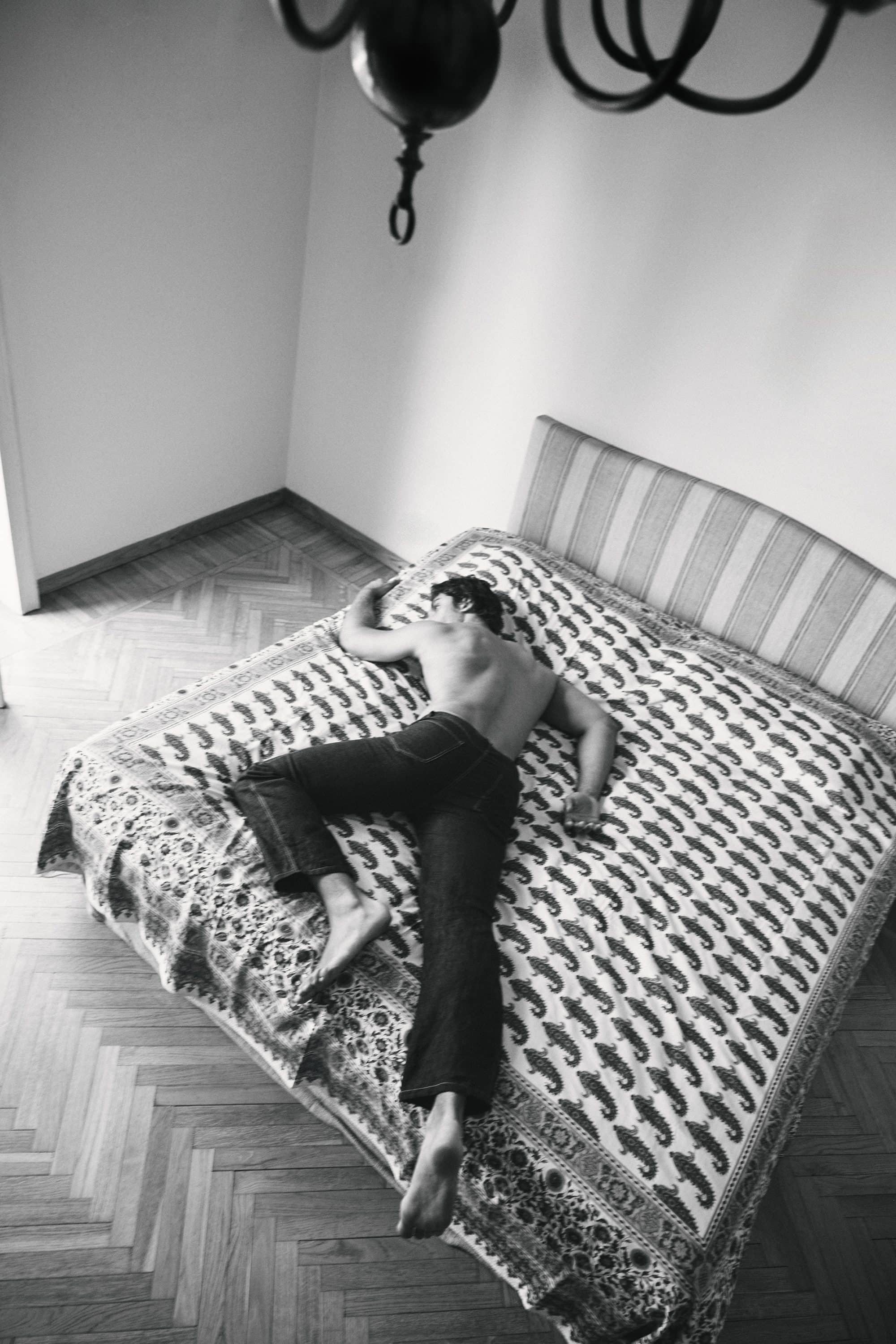 Overhead shot of a man lying face down on a patterned bed in a bedroom for the Taller Marmo 2024 campaign.