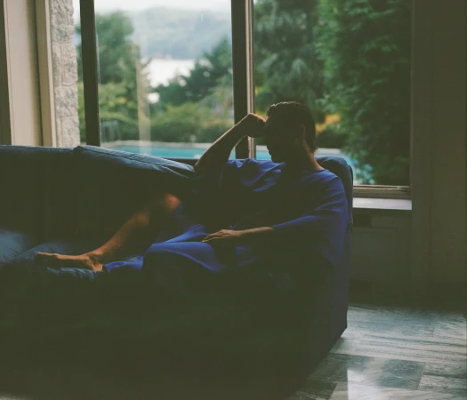 Man relaxing on a blue sofa in front of large windows overlooking a scenic landscape for Taller Marmo campaign.
