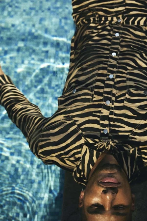 A man wearing a zebra-print long-sleeve shirt lies near a blue tiled swimming pool.