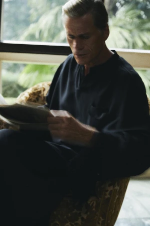 Mark Vanderloo seated reading a newspaper while wearing a black shirt in an interior space for Taller Marmo.