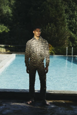 A man wearing a zebra-print matching shirt and trousers standing barefoot beside an outdoor swimming pool.