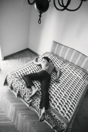 Overhead shot of a man lying face down on a patterned bed in a bedroom for the Taller Marmo 2024 campaign.