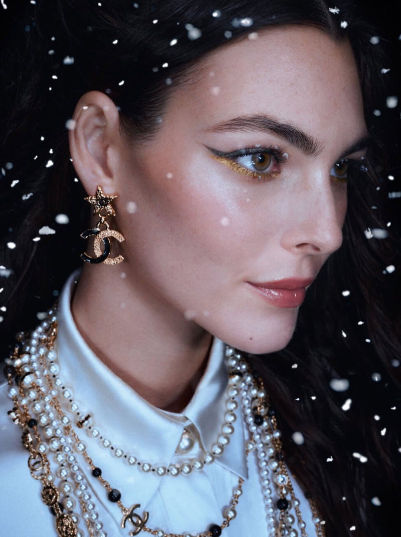 Close-up profile of model Vittoria Ceretti wearing pearl necklaces and star earrings against a dark background with falling snow.