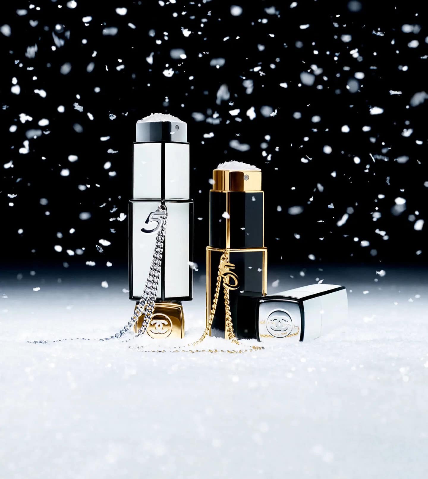 Chanel fragrance bottles standing upright in a snowy white surface against a dark background with falling snow.