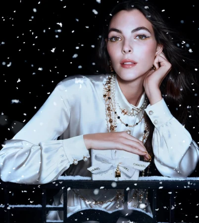 Model Vittoria Ceretti wearing a white silk blouse and pearl necklaces holding a Chanel gift box in falling snow
