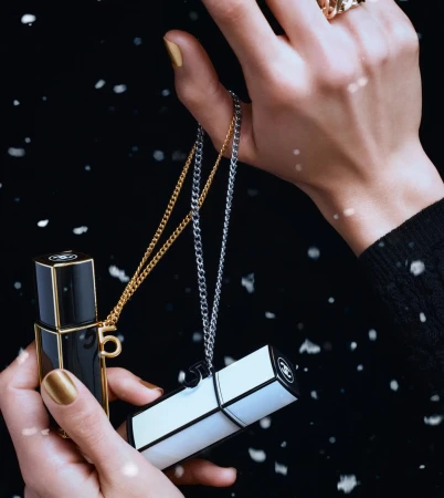 Close-up of hands holding black and white perfume bottles with chains against a dark snowy background.