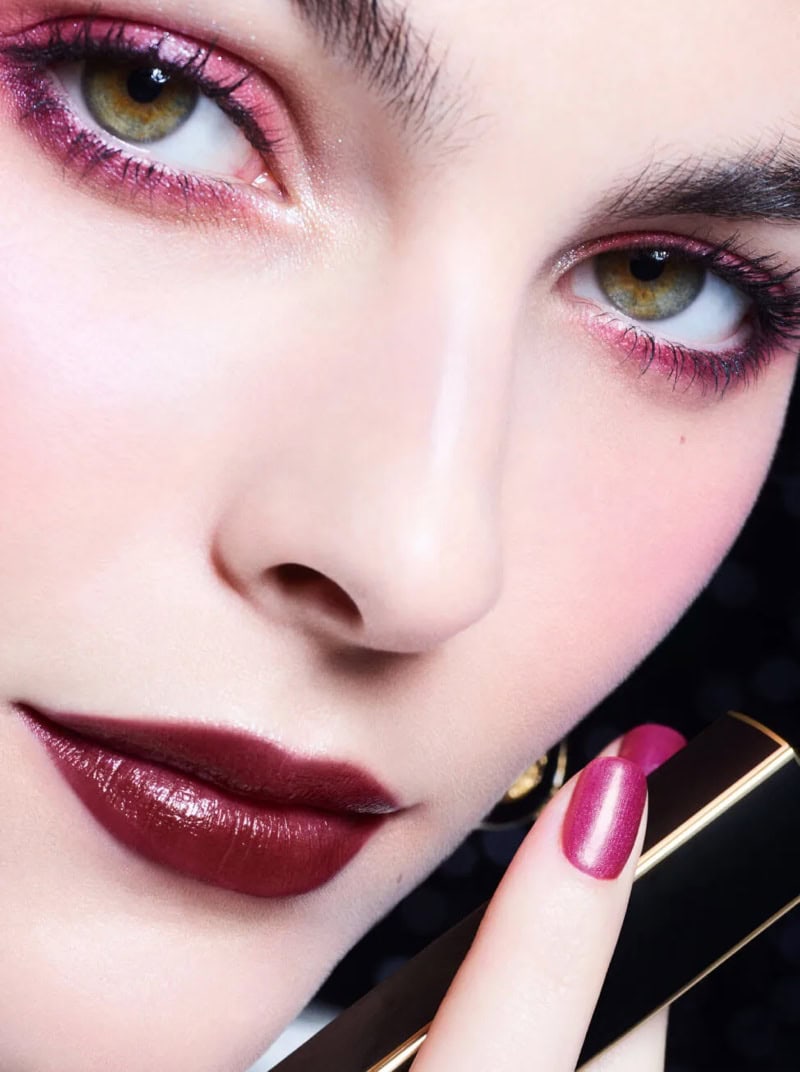 Close-up beauty portrait of model Vittoria Ceretti wearing dark lipstick and pink eyeshadow holding a lipstick tube for Chanel