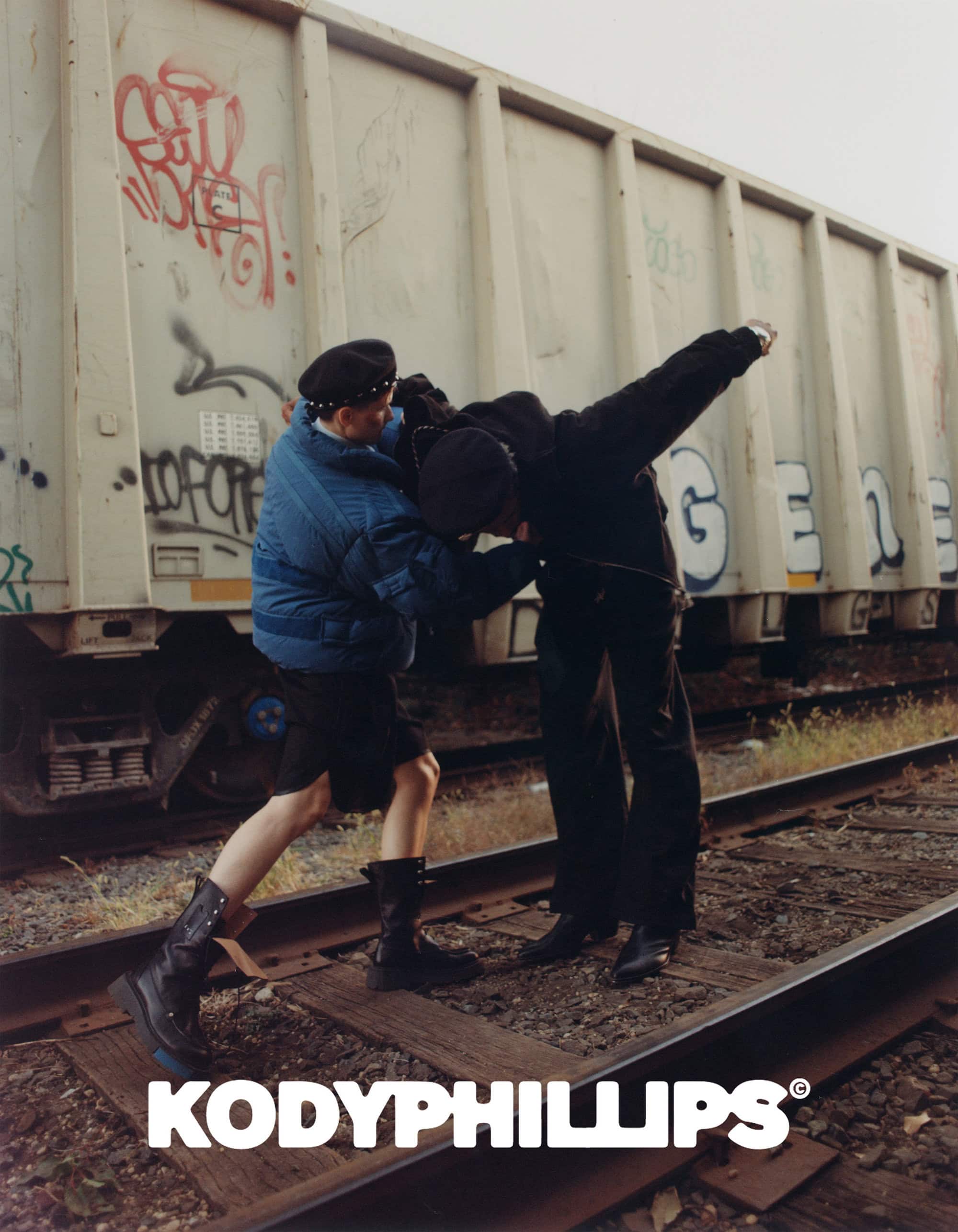 Two models posing on railroad tracks in front of a freight car for Kody Phillips