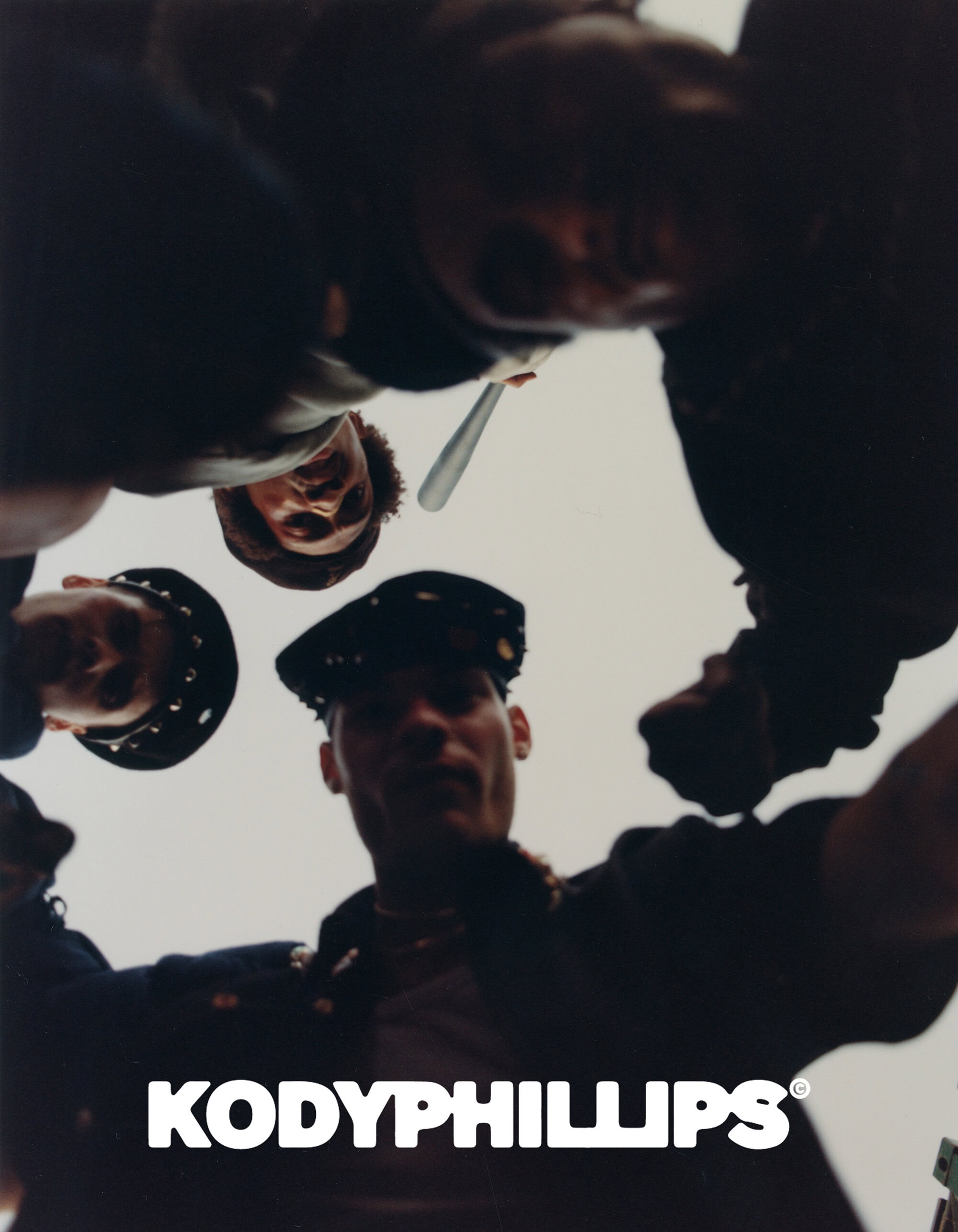 Low angle worm's-eye view looking up at a group of men surrounding the camera holding props against an overcast sky