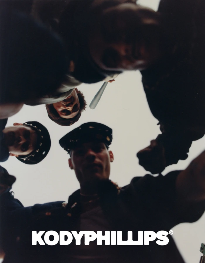 Low angle worm's-eye view looking up at a group of men surrounding the camera holding props against an overcast sky