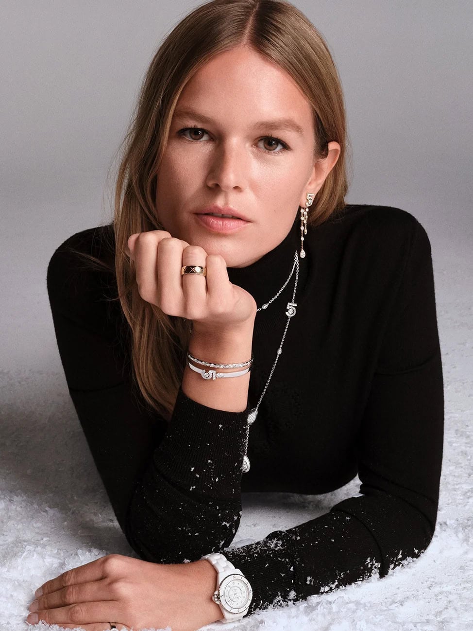 Model Anna Ewers wearing fine jewelry and a black turtleneck against a snowy studio backdrop for Chanel