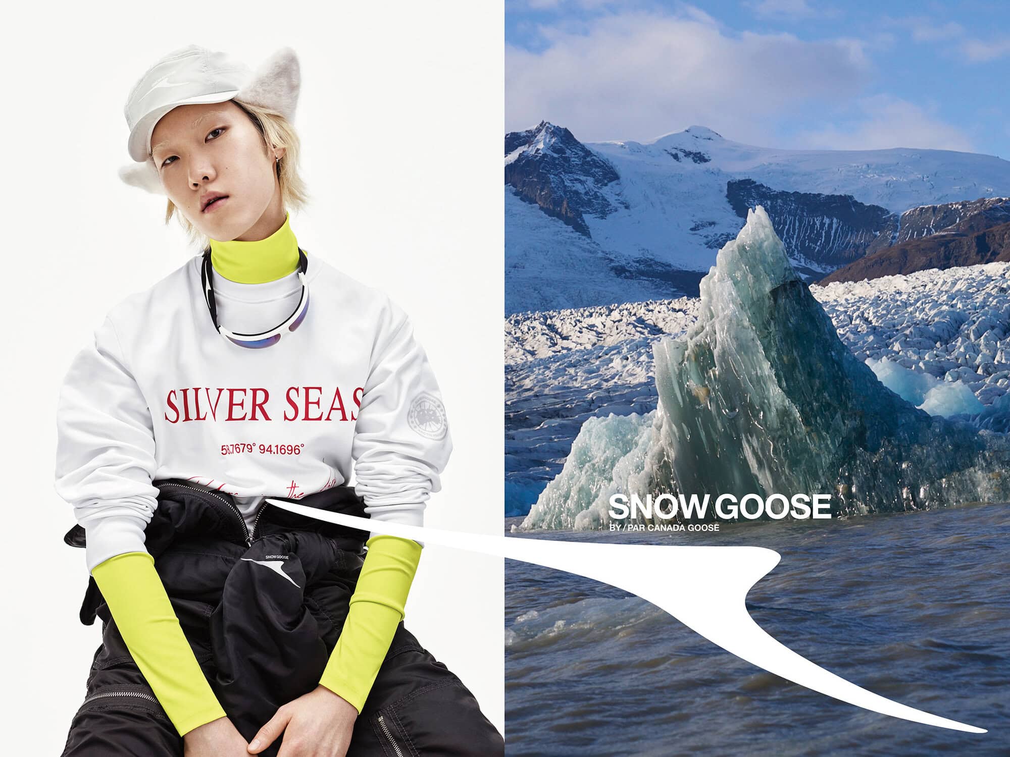 Model wearing a white sweatshirt with silver seas typography and a yellow turtleneck against a white seamless background beside a snowy mountain landscape