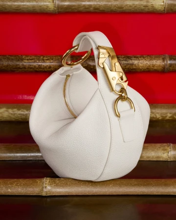 White leather handbag with gold hardware displayed against a red background and horizontal bamboo stalks