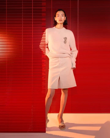 Model in cream knit sweater and skirt standing against bright red slatted blinds for Burberry Year of the Snake campaign