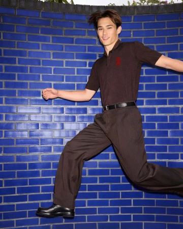 Man wearing a brown polo shirt and trousers posing against a blue brick wall in a Burberry campaign