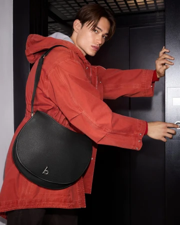 Young man in red jacket wearing a black leather shoulder bag pressing an elevator button.
