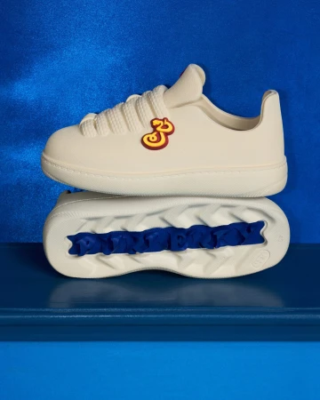 Two off-white sneakers stacked vertically against a vibrant blue textured background for Burberry Year of the Snake campaign