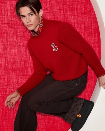 Man wearing a red sweater and dark trousers posed against a textured red circular backdrop for Burberry