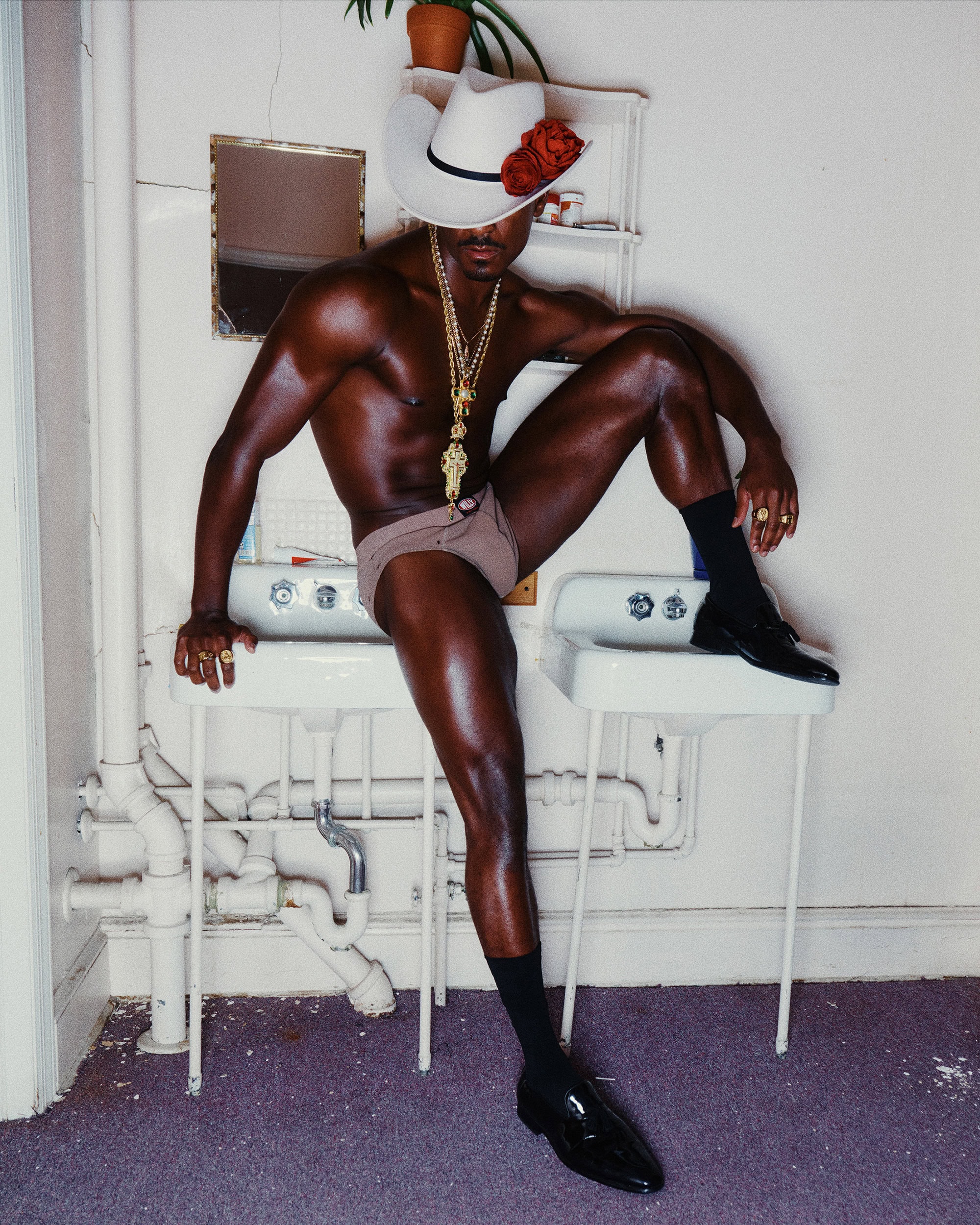 Man wearing a white cowboy hat with red roses perched on double sinks in a bathroom for Willy Chavarria Fall 2024 Ad Campaign.