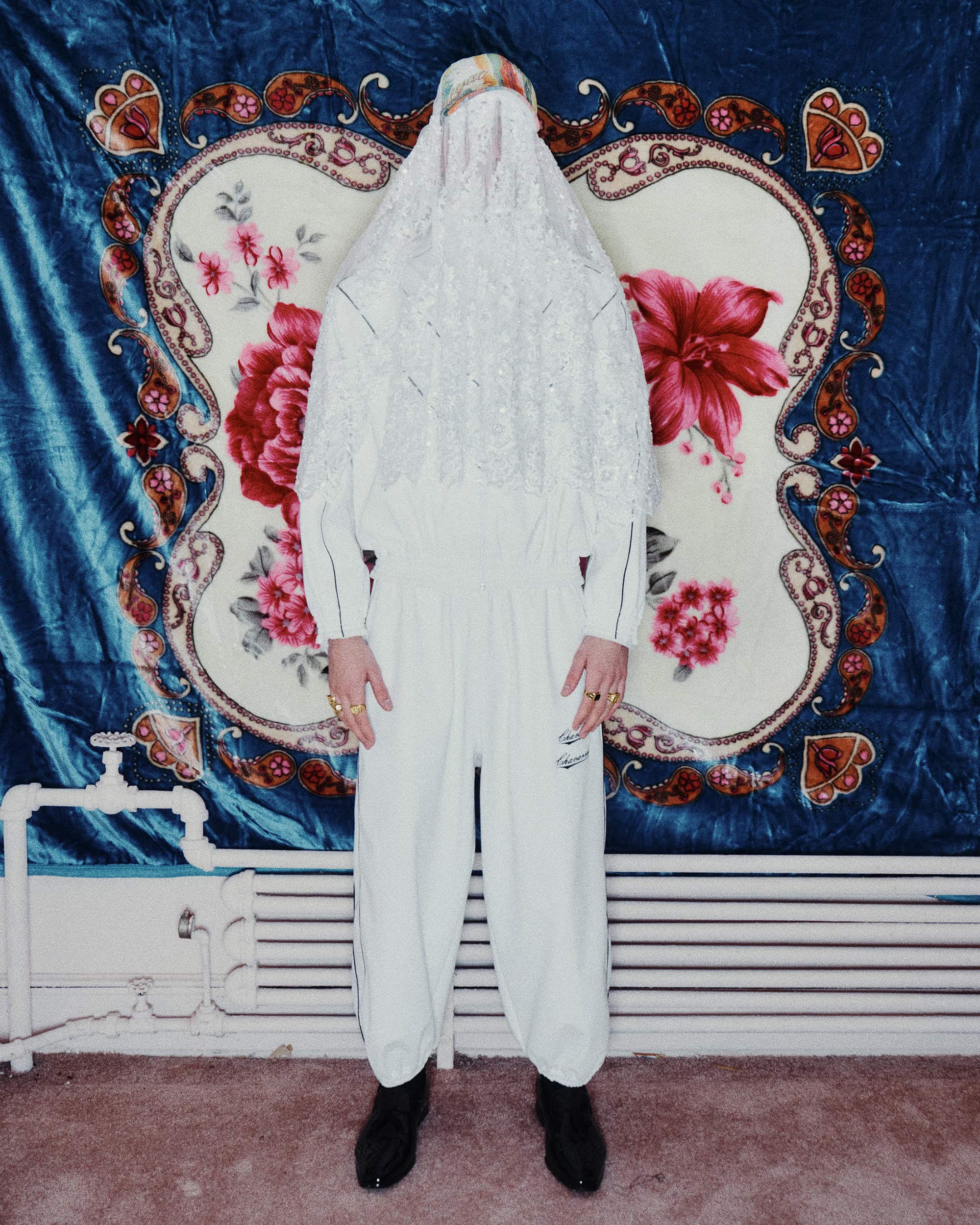Model wearing a white hooded lace cover-up and matching white tracksuit standing against a patterned floral backdrop.