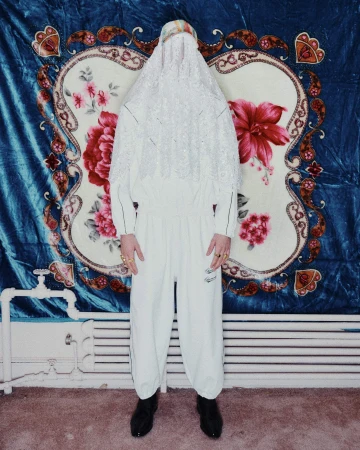 Model wearing a white hooded lace cover-up and matching white tracksuit standing against a patterned floral backdrop.