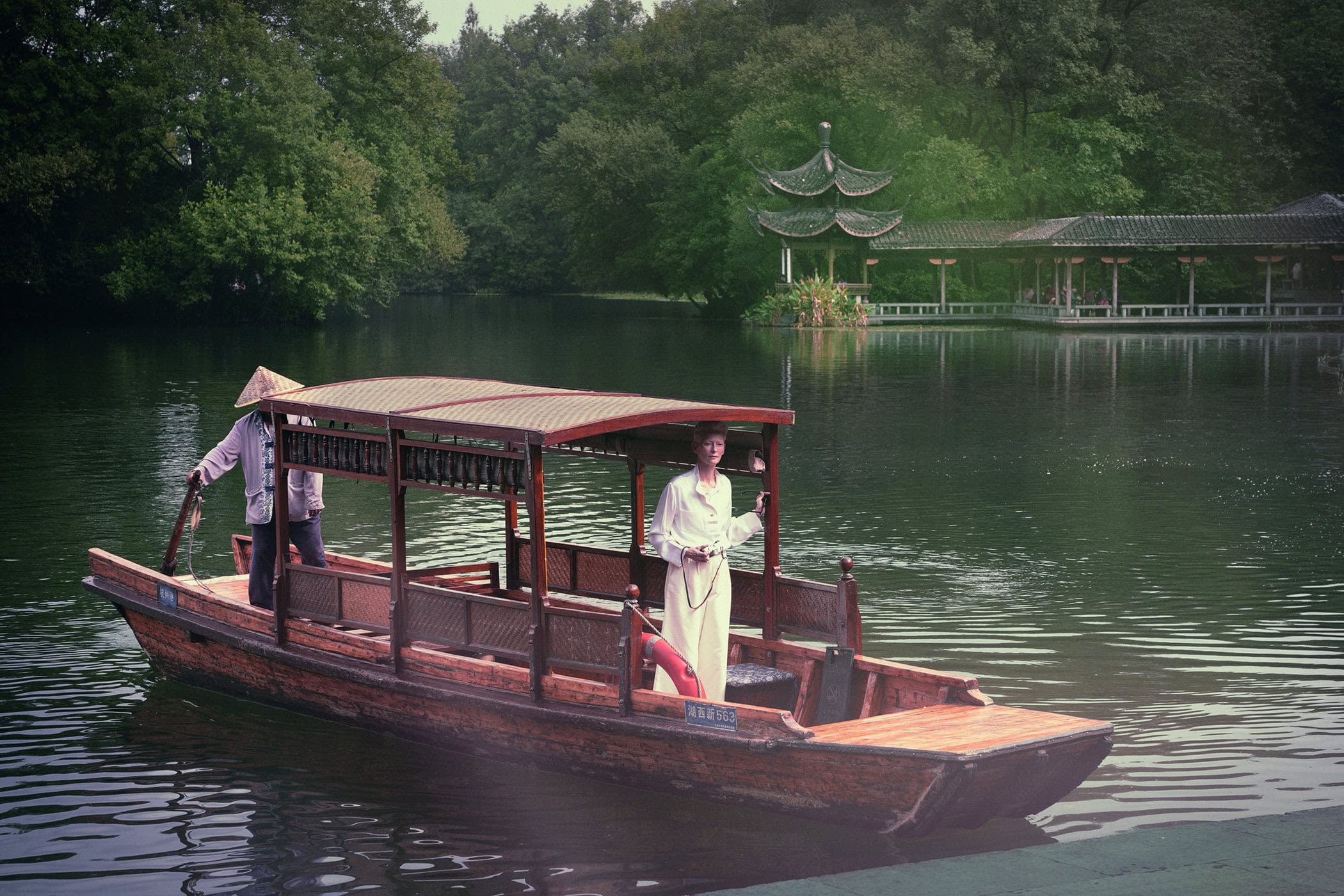 Tilda Swinton on a traditional wooden boat on a serene lake with an Asian pagoda pavilion in the background for Chanel