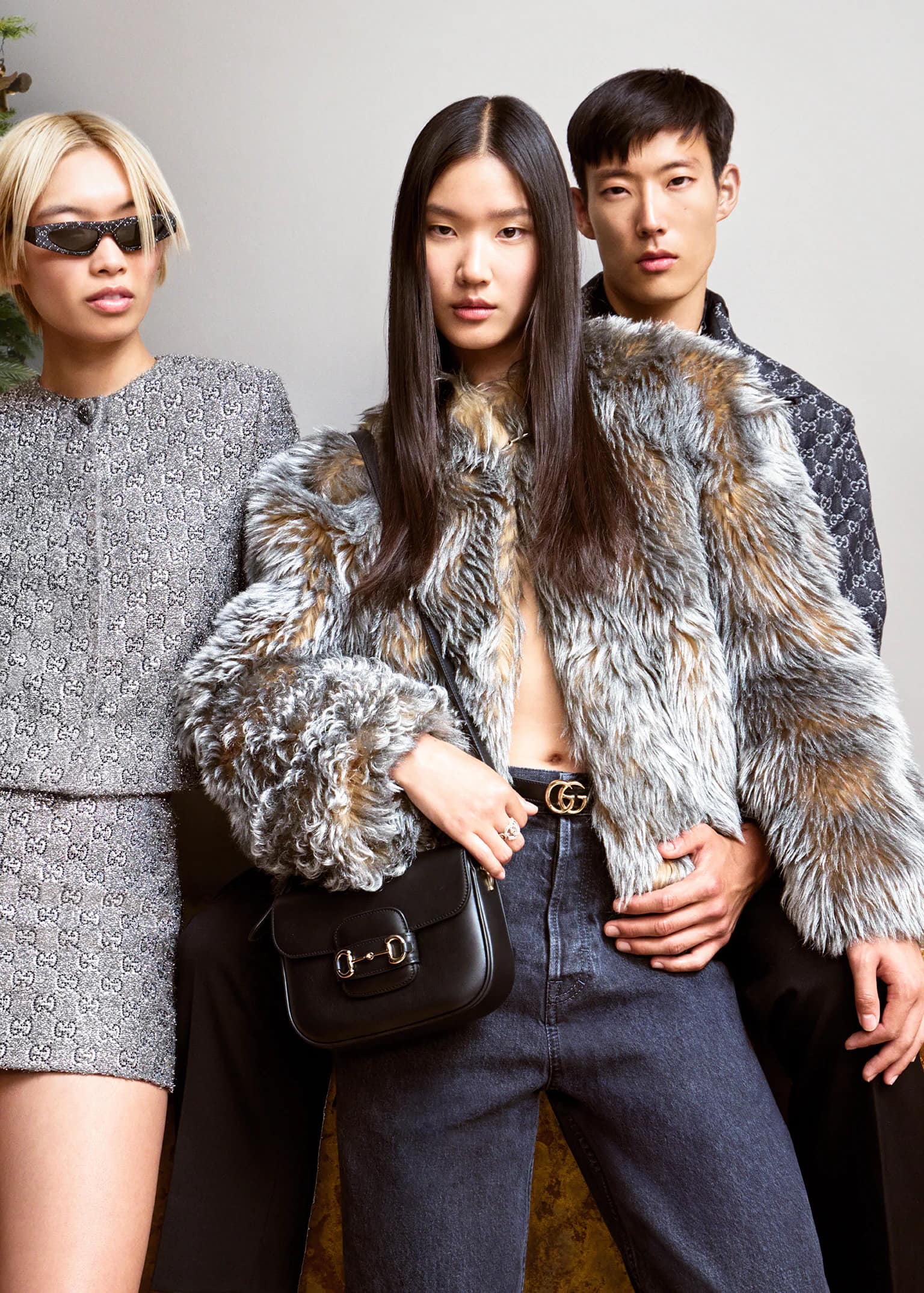 Three models wearing Gucci apparel against a plain light background, featuring a patterned jacket and black shoulder bag
