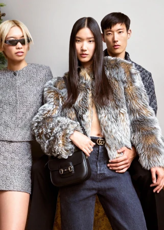 Three models wearing Gucci apparel against a plain light background, featuring a patterned jacket and black shoulder bag