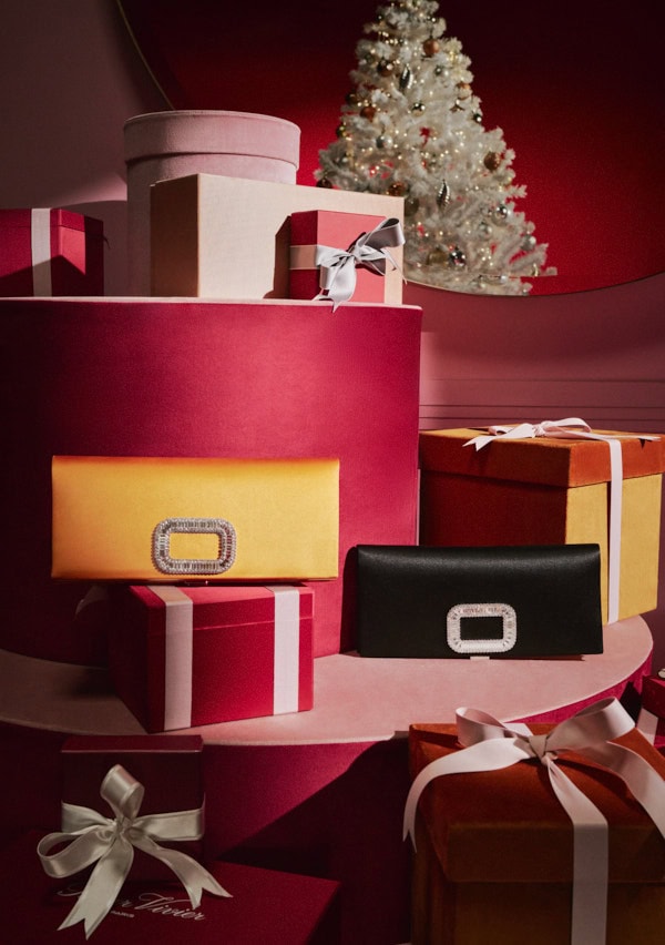 Stacked luxury gift boxes and satin clutches with crystal buckles in a festive holiday display with a small white tree