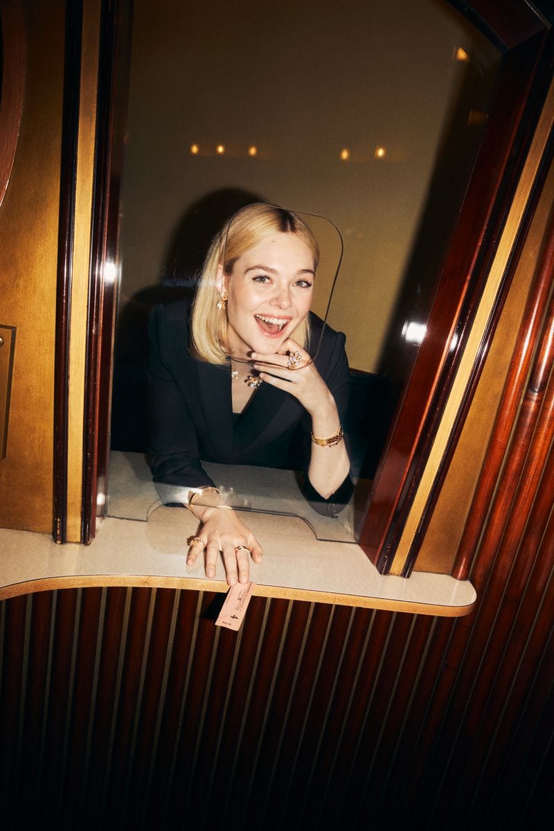 Elle Fanning leaning over a ticket counter in a dark wood interior for Cartier Fall 2024 ad campaign