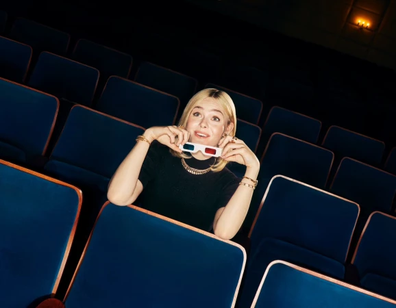 Elle Fanning holding 3D glasses in a dark cinema filled with empty blue theatre seats for Cartier Fall 2024 campaign